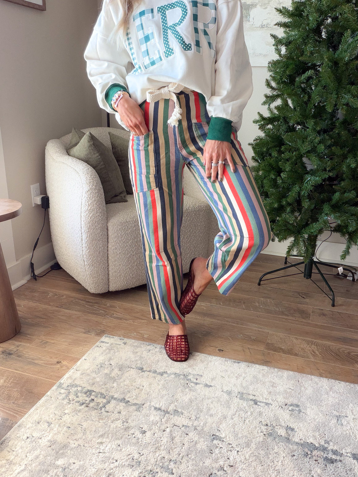 Front view of multicolor striped cotton pants with wide legs and a rope tie, shown with one knee bent.