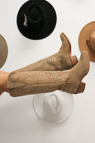 Tan cowboy boots with white stitching on a white background with hats. Tecovas women’s cowboy boots