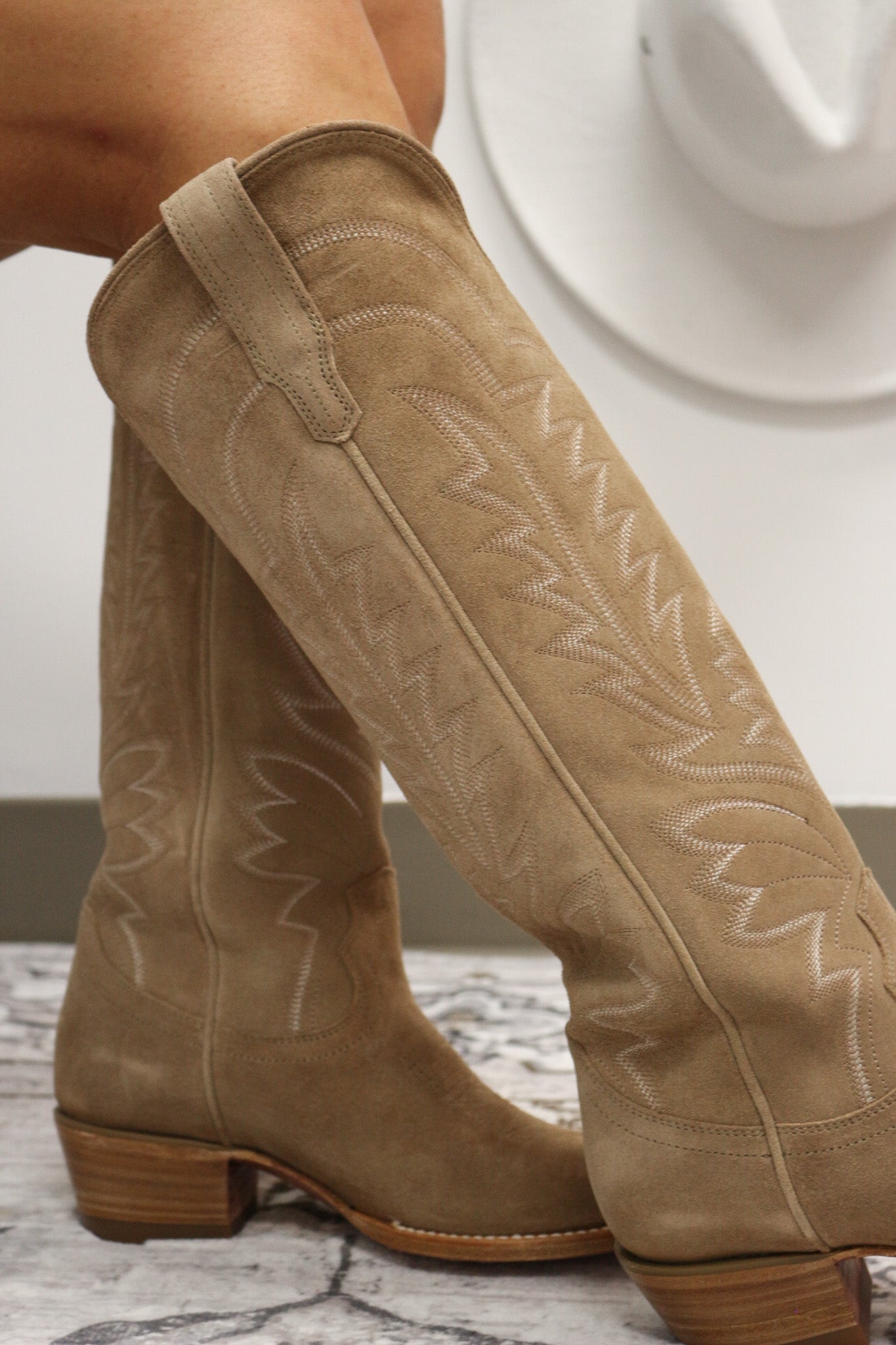 Tan cowboy boots with intricate stitching on a neutral background. Tecovas women’s cowboy boots