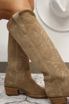 Tan cowboy boots with intricate stitching on a neutral background. Tecovas women’s cowboy boots