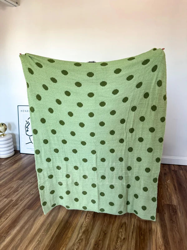 A soft, reversible blanket with pistachio and dark green polka dots displayed spread out.