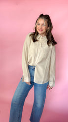 woman standing against pink background modeling barrel jeans and neutral button up long sleeve blouse