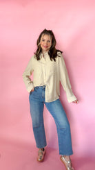 woman standing against pink background modeling barrel jeans and neutral button up long sleeve blouse