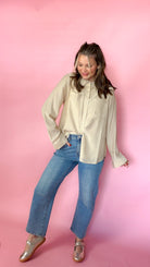 woman standing against pink background modeling barrel jeans and neutral button up long sleeve blouse