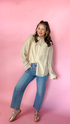 woman standing against pink background modeling barrel jeans and neutral button up long sleeve blouse