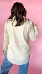 woman standing against pink background modeling barrel jeans and neutral button up long sleeve blouse