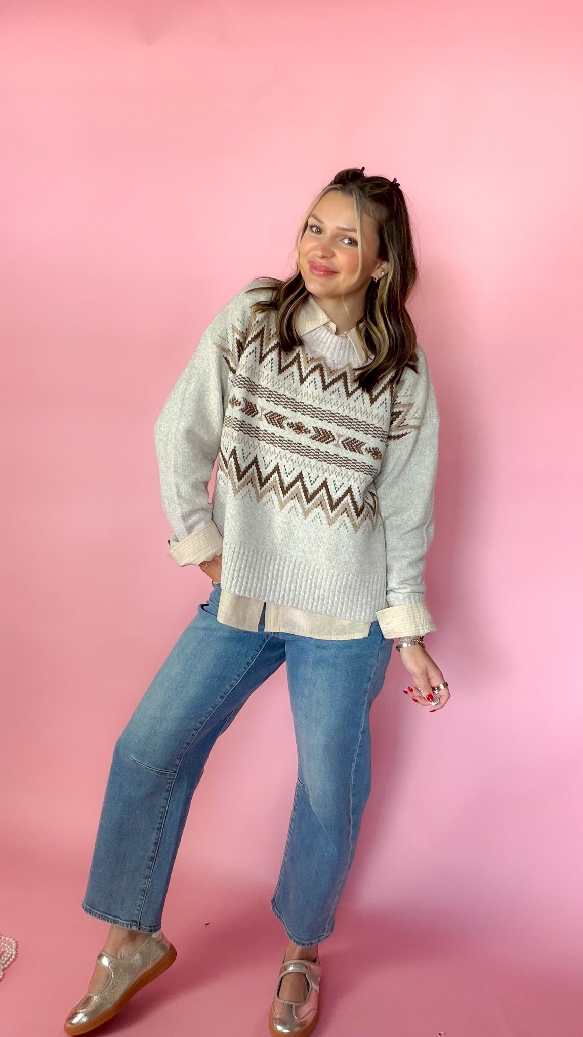 woman standing against pink background modeling barrel jeans and neutral button up long sleeve blouse