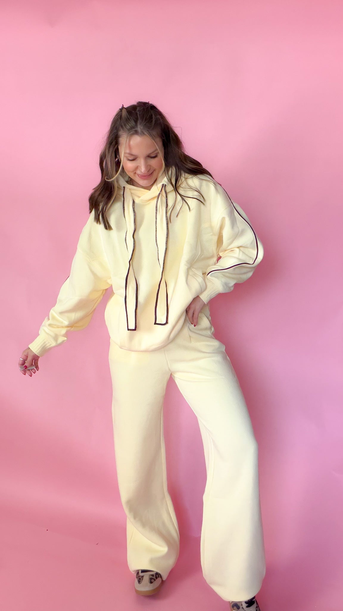 woman standing against pink background with yellow hoodie and sweatpants matching set