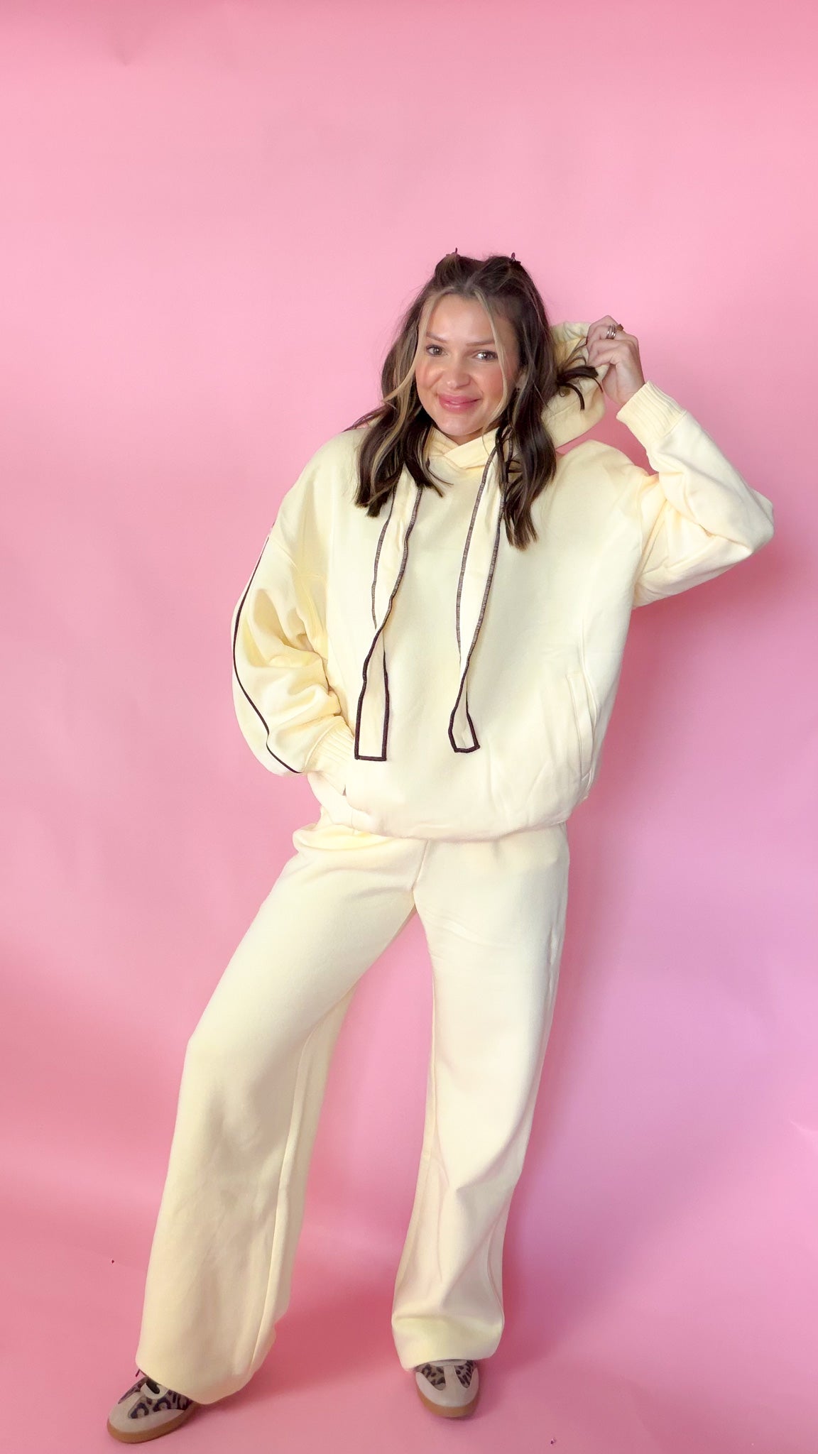 woman standing against pink background with yellow hoodie and sweatpants matching set
