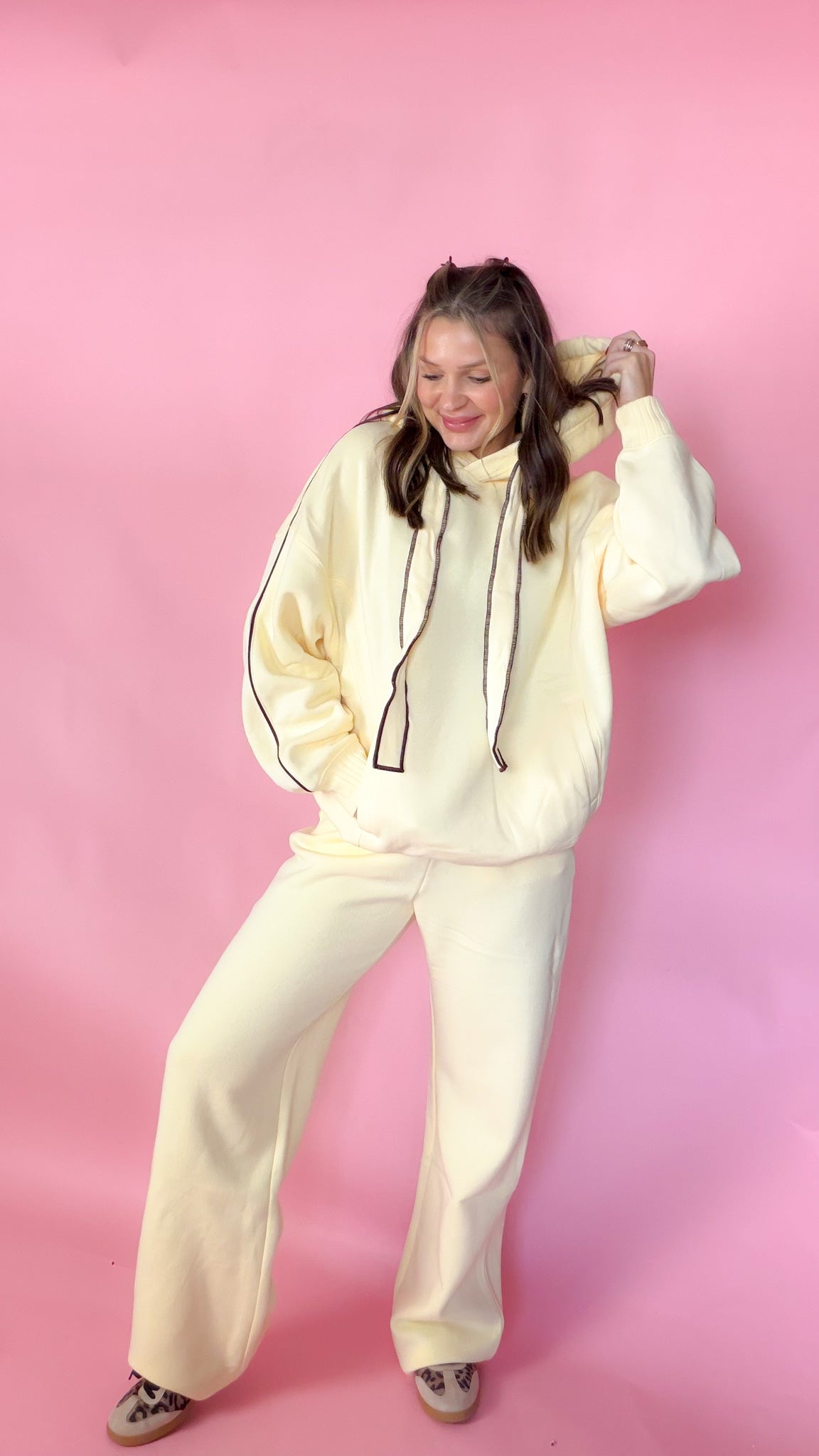woman standing against pink background with yellow hoodie and sweatpants matching set