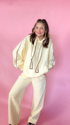 woman standing against pink background with yellow hoodie and sweatpants matching set