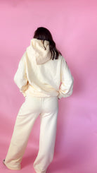 woman standing against pink background with yellow hoodie and sweatpants matching set