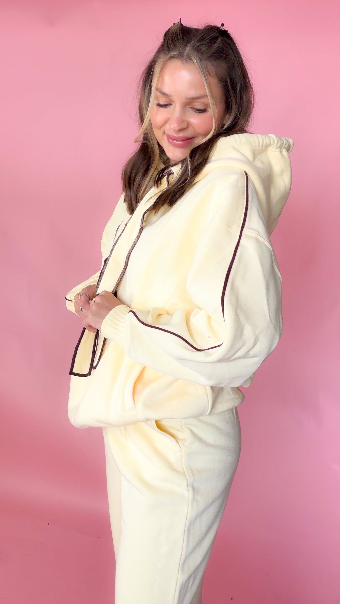 woman standing against pink background with yellow hoodie and sweatpants matching set