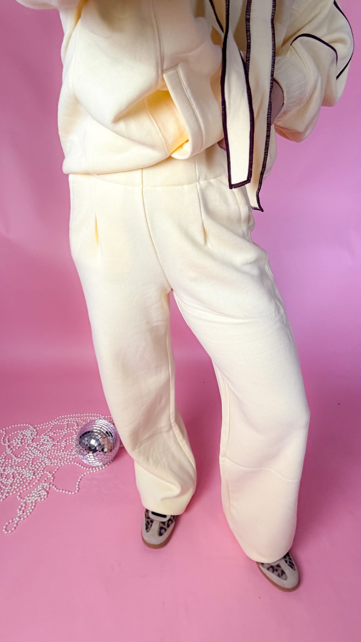 woman standing against pink background with yellow hoodie and sweatpants matching set
