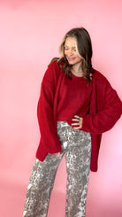 woman wearing a red knit tank with a matching red cardigan against a pink background. Paired with snake print pants
