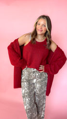 woman wearing a red knit tank with a matching red cardigan against a pink background. Paired with snake print pants