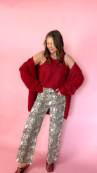 woman wearing a red knit tank with a matching red cardigan against a pink background. Paired with snake print pants