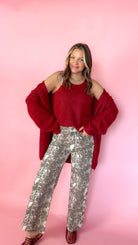 woman wearing a red knit tank with a matching red cardigan against a pink background. Paired with snake print pants