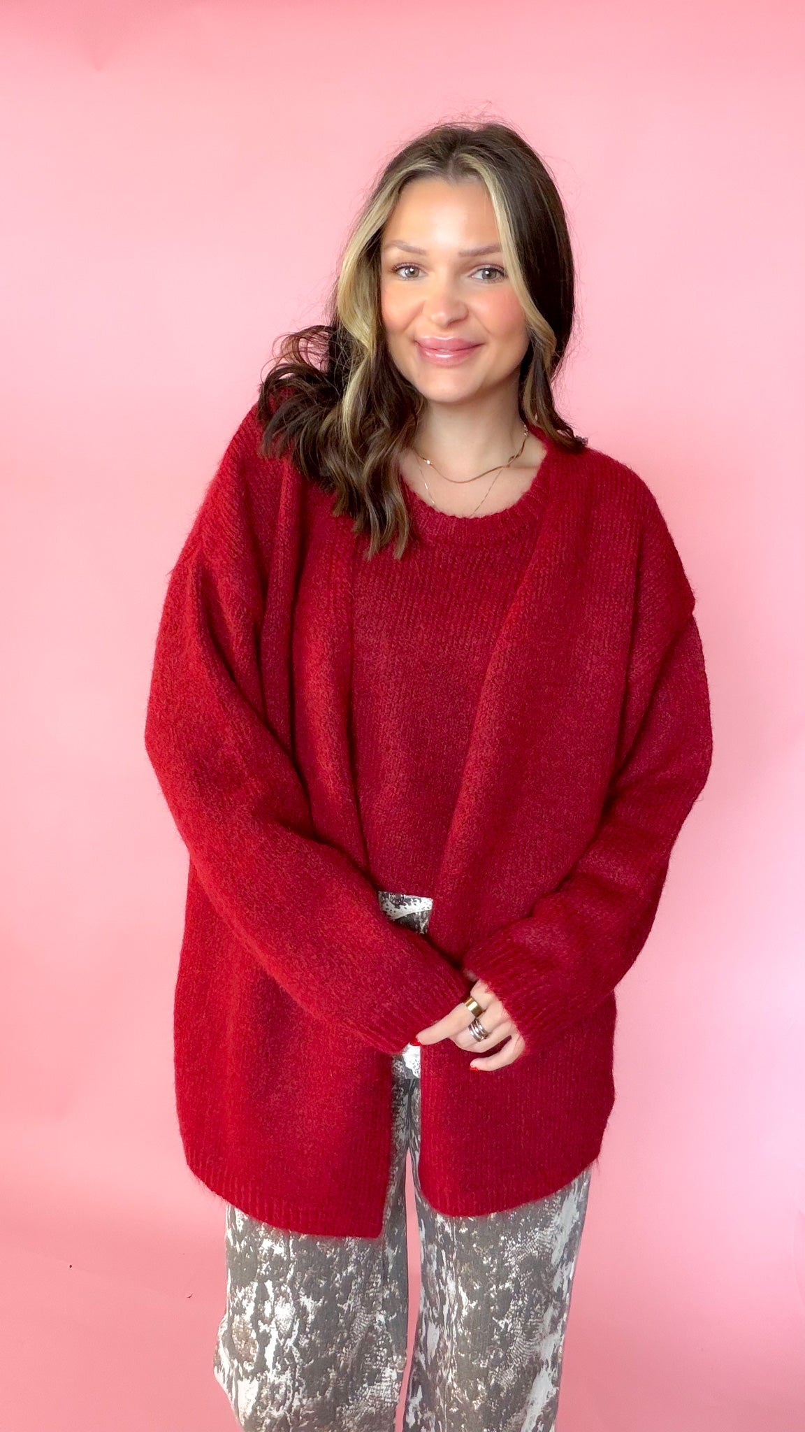 woman wearing a red knit tank with a matching red cardigan against a pink background. Paired with snake print pants