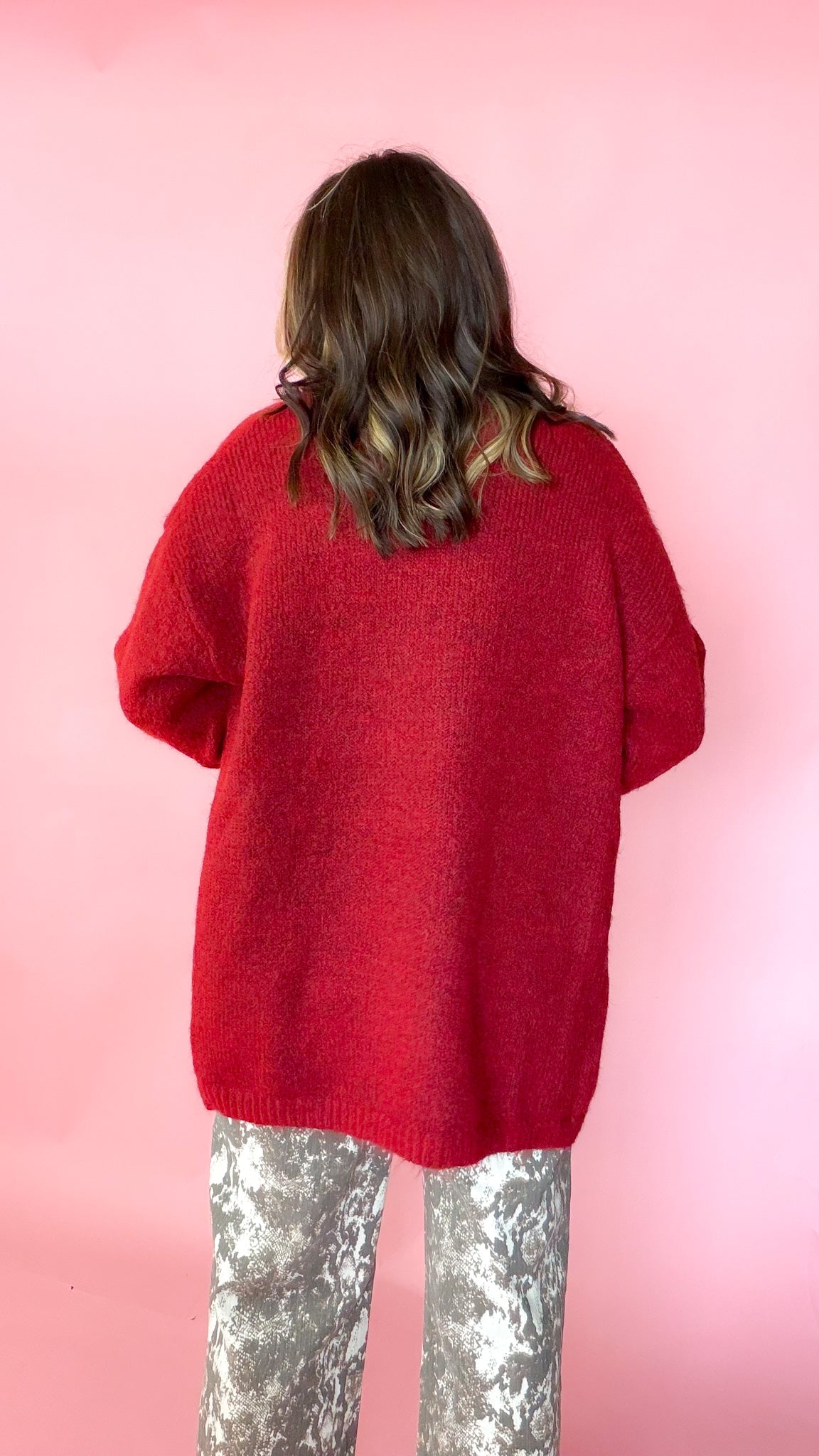 woman wearing a red knit tank with a matching red cardigan against a pink background. Paired with snake print pants