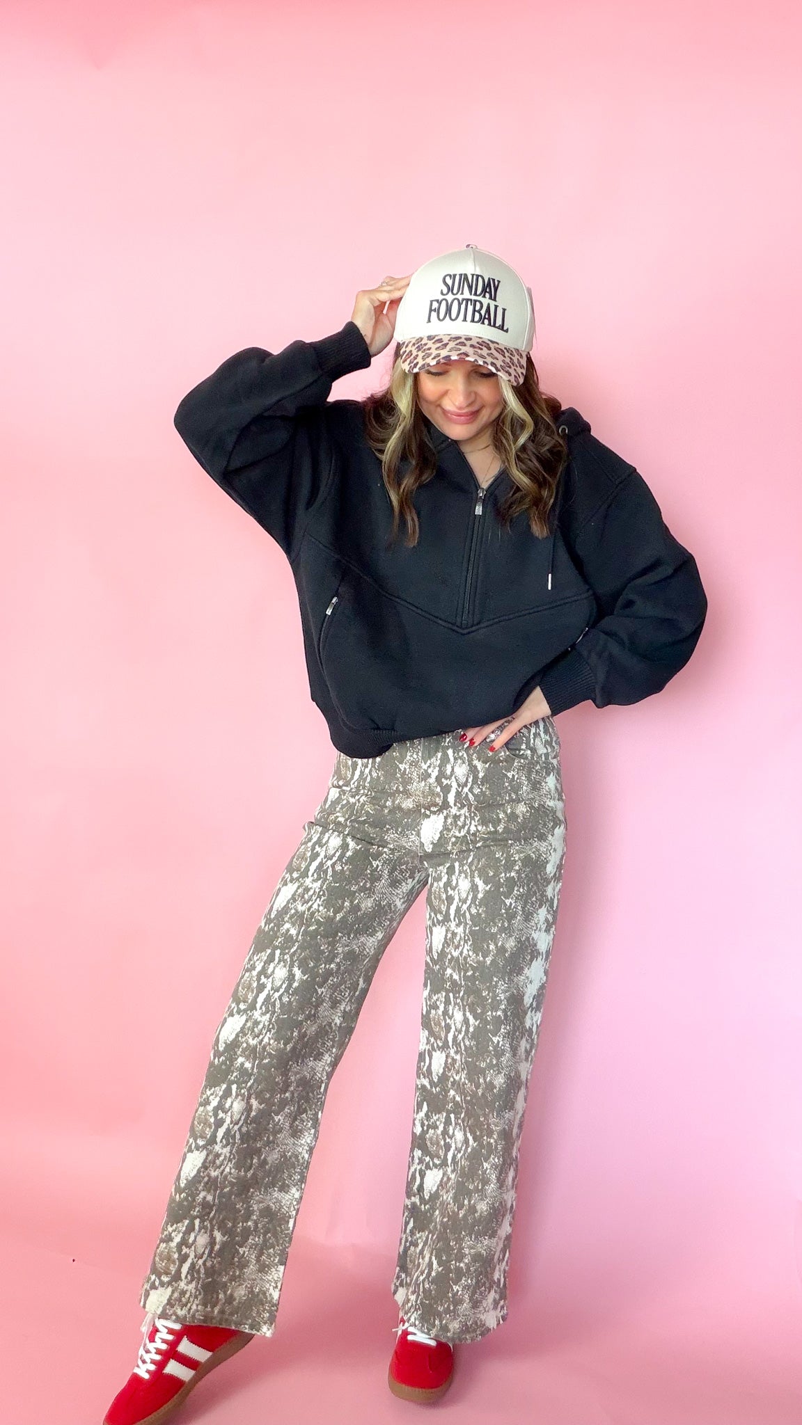 woman picturing black half zip pullover with leopard trucker hat and snake print jeans.