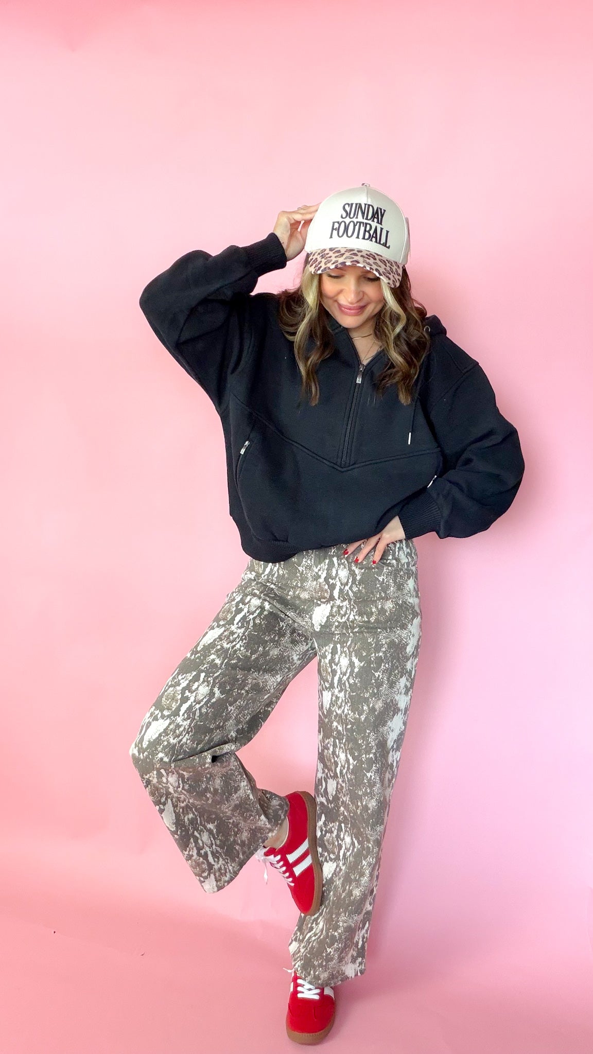 woman picturing black half zip pullover with leopard trucker hat and snake print jeans.