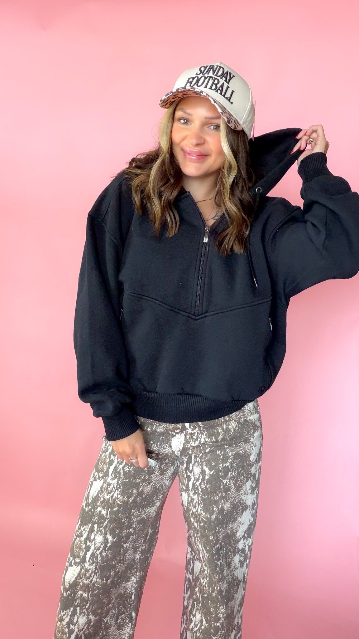 woman picturing black half zip pullover with leopard trucker hat and snake print jeans