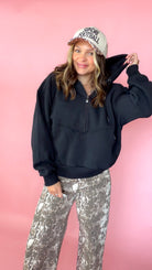 woman picturing black half zip pullover with leopard trucker hat and snake print jeans
