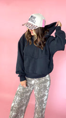 woman picturing black half zip pullover with leopard trucker hat and snake print jeans.