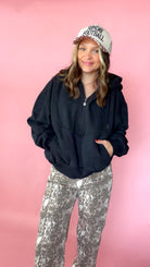 woman picturing black half zip pullover with leopard trucker hat and snake print jeans.