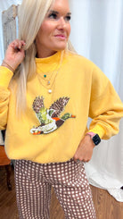 A woman wearing a yellow sweatshirt with a large embroidered duck graphic on the front, paired with brown and white gingham pants.