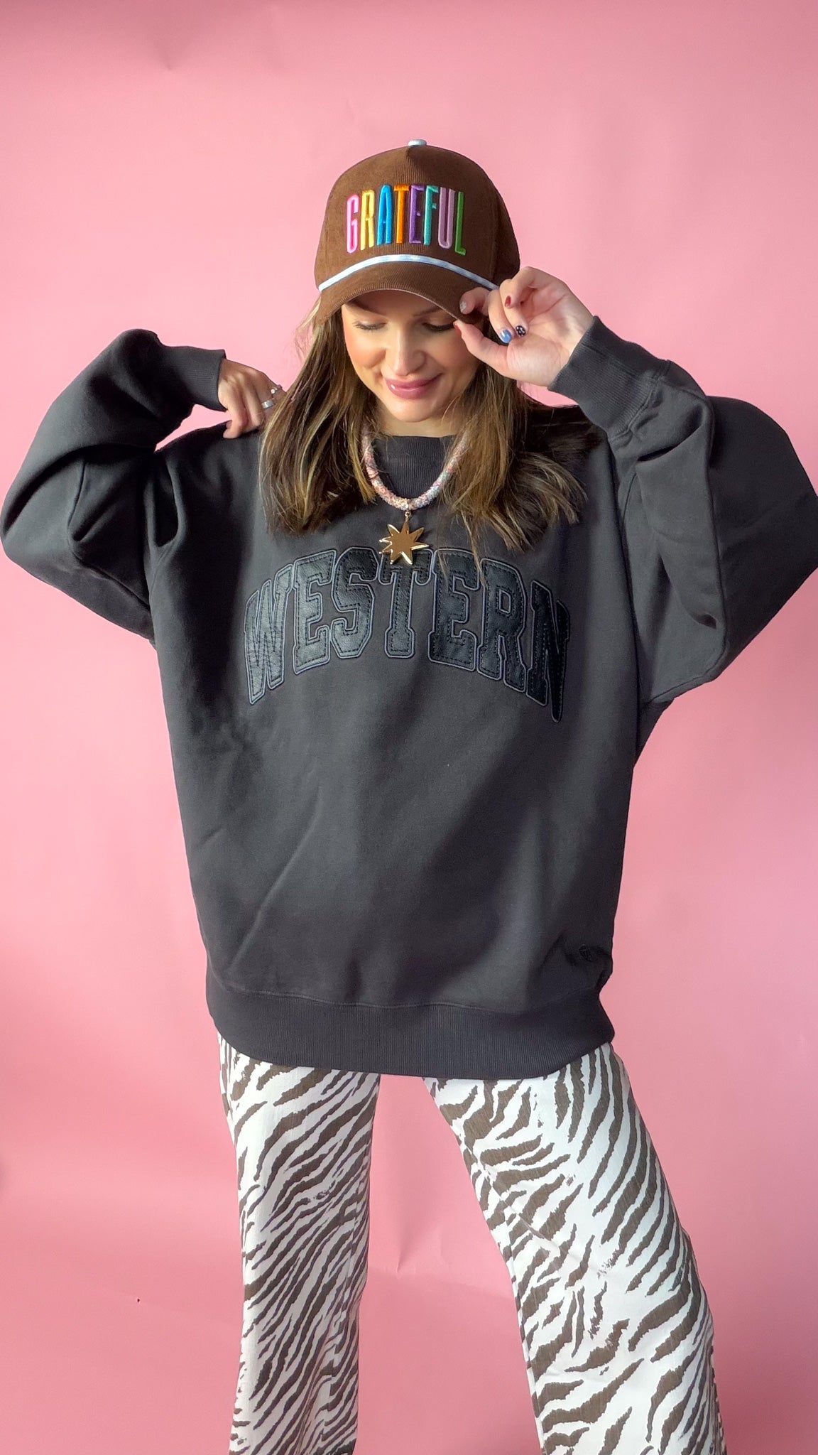 woman wearing ariat western oversized sweatshirt paired with a brown trucker hat and zebra pants