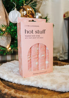Lemon Lavender Hot Stuff Heated Neck Wrap in light pink, boxed by a Christmas tree