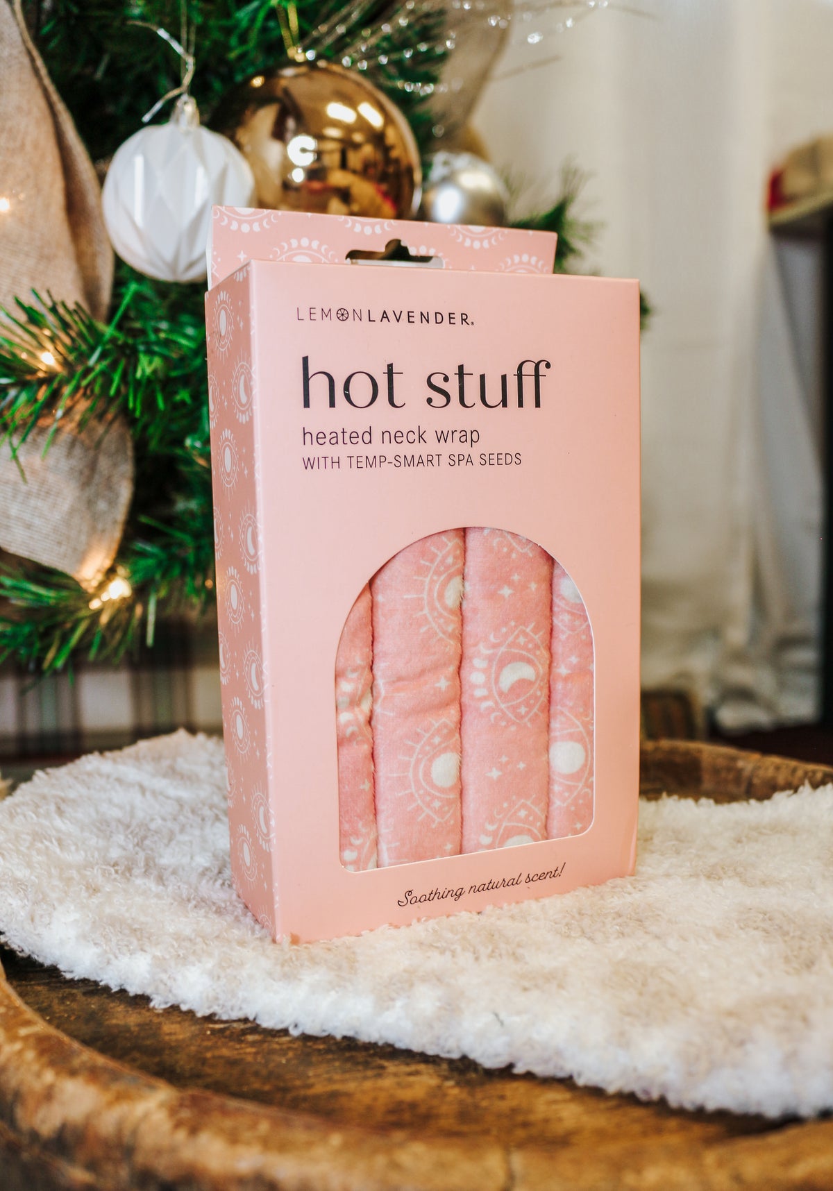 Lemon Lavender Hot Stuff Heated Neck Wrap in light pink, boxed by a Christmas tree
