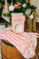 Hot Stuff Heated Neck Wrap in light pink, wrap draped over a barrel in front of its box