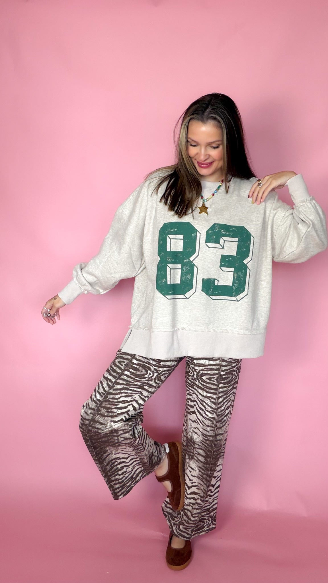 Keeping Score oatmeal sweatshirt with green 83 graphic worn with zebra print pants, playful pose