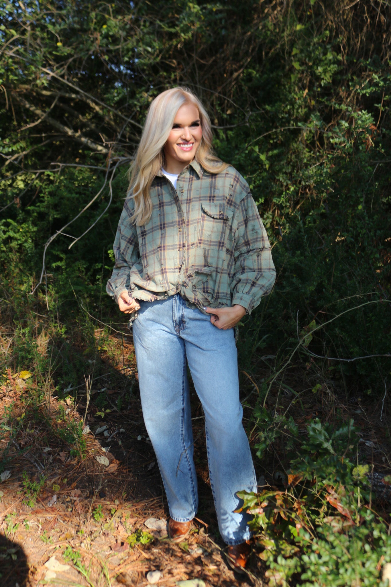 Woman wearing a plaid shirt and jeans standing in a forested area