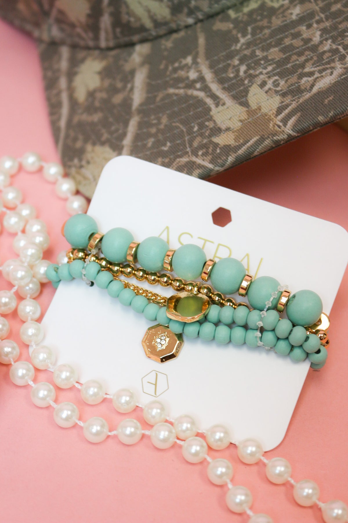 Charlie Paige Mayan teal bracelet set on its Astral card, styled with pearls and a camo cap