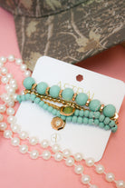 Charlie Paige Mayan teal bracelet set on its Astral card, styled with pearls and a camo cap