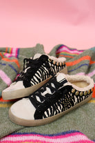Women's Pippa zebra print slip-on sneakers with black laces and sherpa lining, pair on a striped blanket