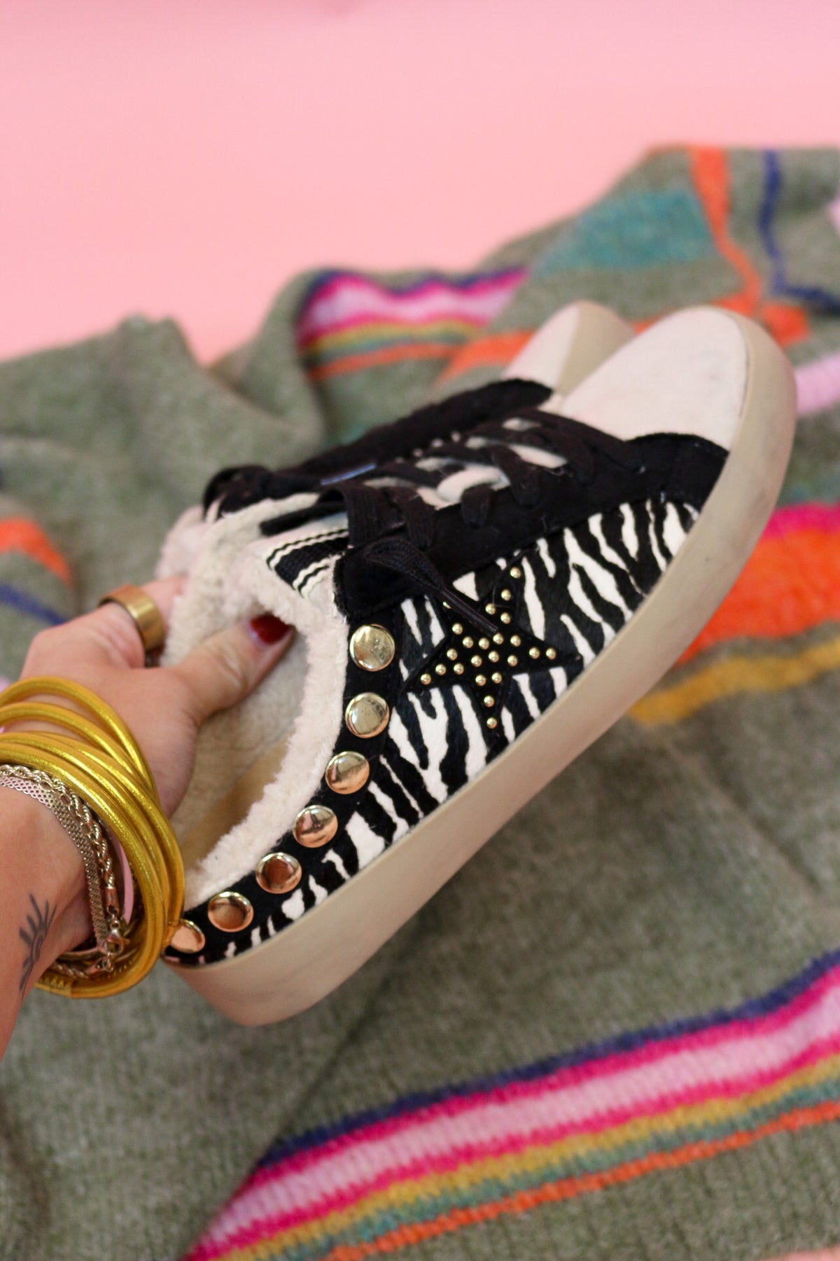 Hand holding a Pippa zebra slip-on sneaker, side view showing the gold-studded heel