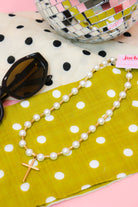 Lolly Pearl Beaded Gold Cross Necklace, full length flat lay with a disco ball and sunglasses