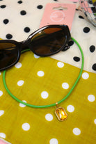 Quin Pendant Necklace in green cord with yellow jewel pendant beside sunglasses