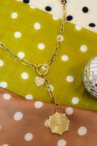 Laney Lariat Gold Charm Necklace on green and tan polka dot fabric with a disco ball
