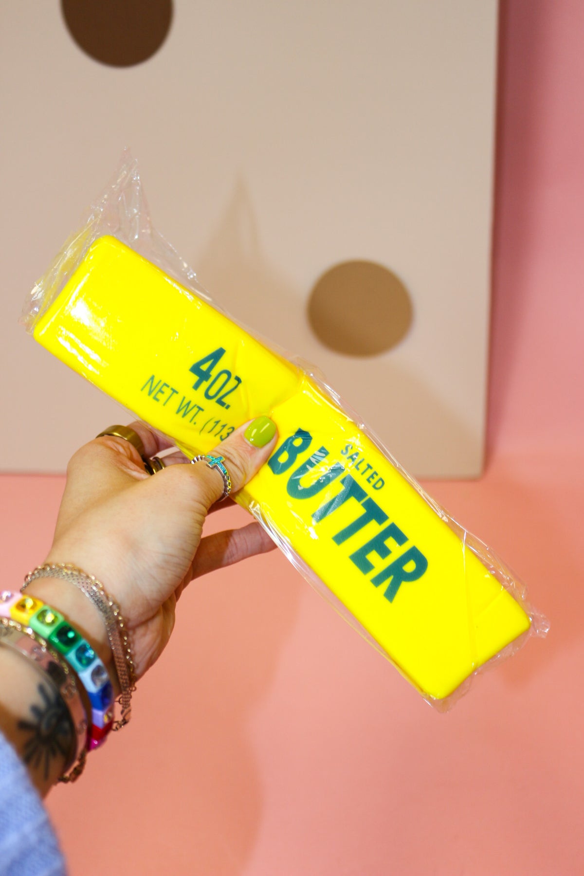 Hand squeezing a large yellow butter-stick squishy with green Salted Butter lettering inside clear packaging.