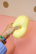 Hand holding and squeezing a pale golden-tan jumbo peanut squishy with raised shell-like texture.