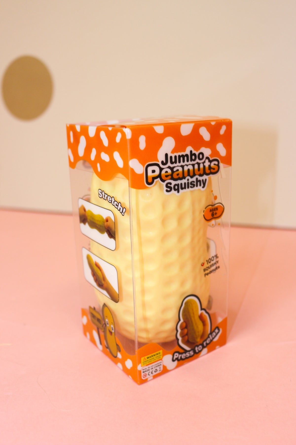 Jumbo peanut squishy in clear packaging with orange-and-white Jumbo Peanuts Squishy branding on a pink surface.