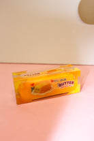 Butter squishy toy in a yellow rectangular box with butter-themed graphics displayed on a pink surface.