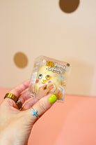 Hand holding a yellow egg squishy toy in clear Egg Shaped Squishy packaging against a dotted backdrop.