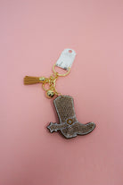 Brown rhinestone cowboy boot keychain charm with brown tassel and gold-tone key ring on a pink background